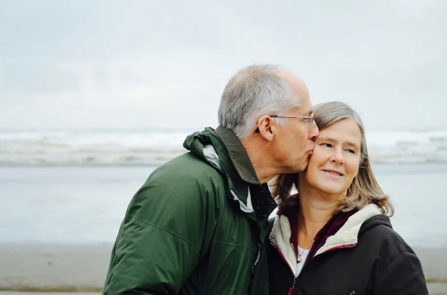 A retired man kissing his wife on the cheek on the beach